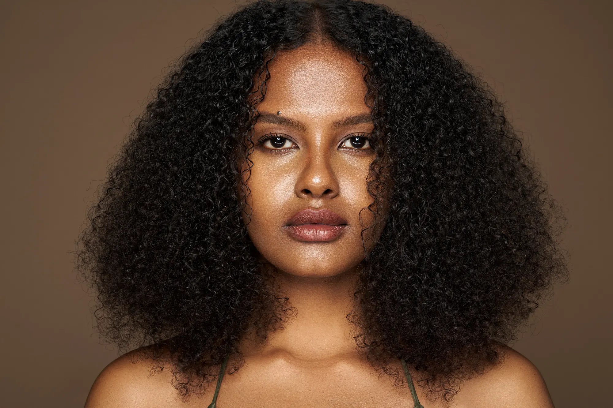 Woman with curly hair against a brown background