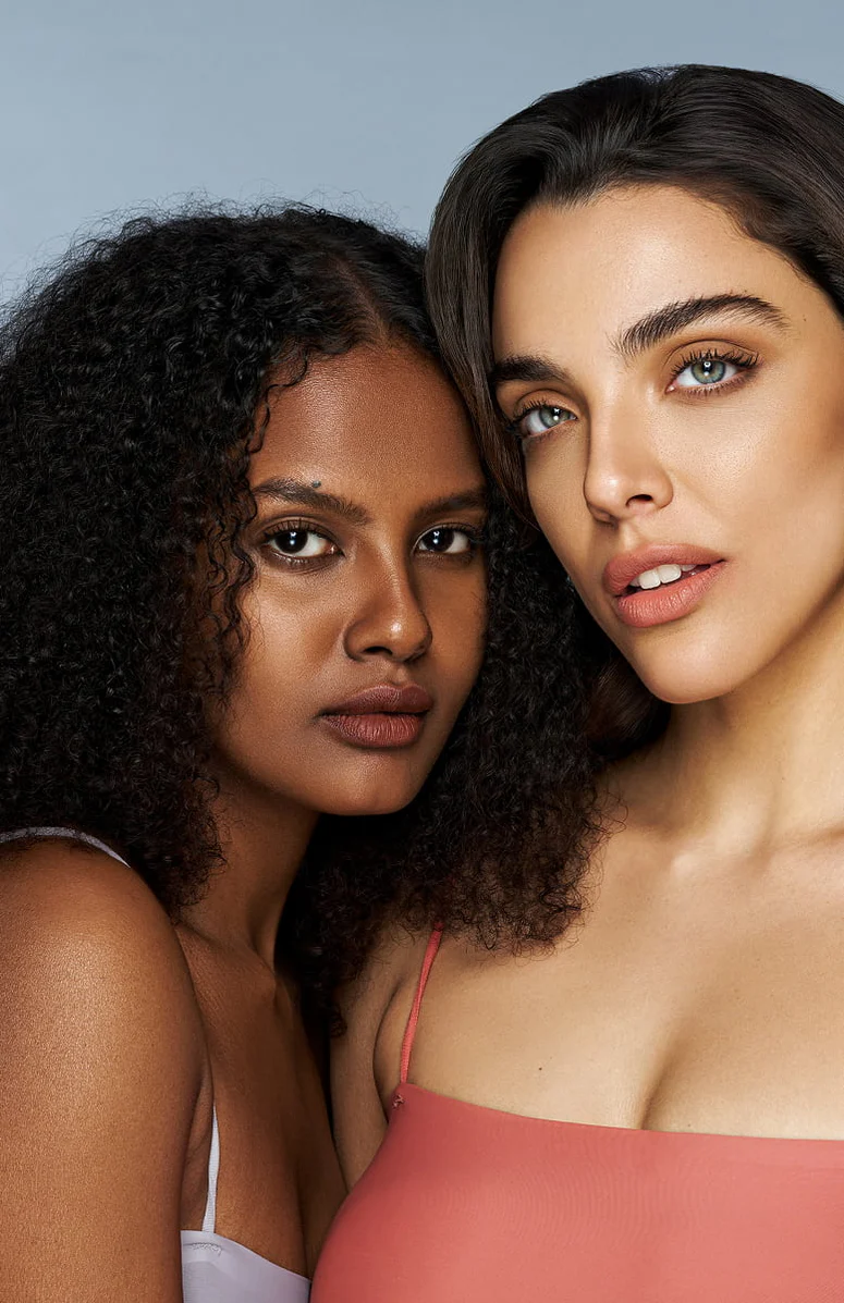 Two women posing closely together against a neutral background