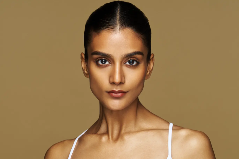 Woman wearing a white tank top against a brown background