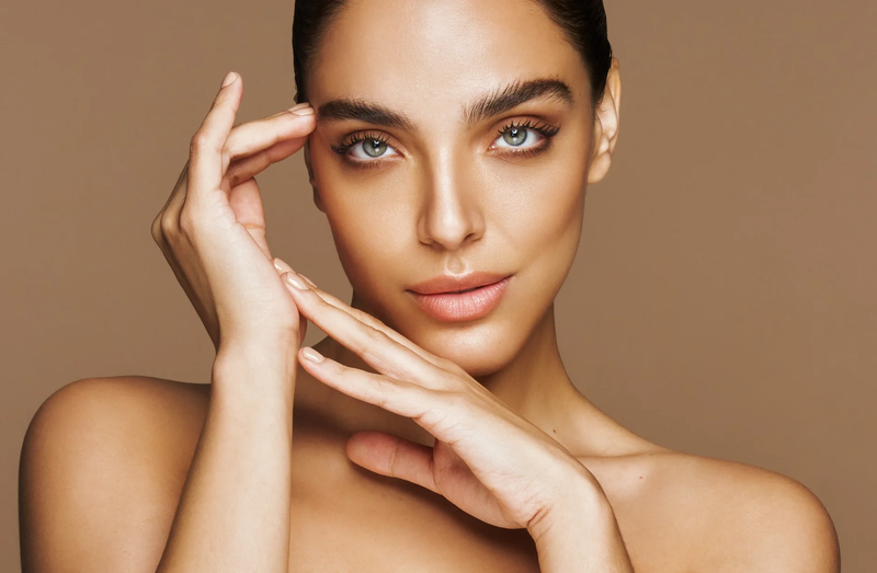Woman with clear skin touching her face against a brown background