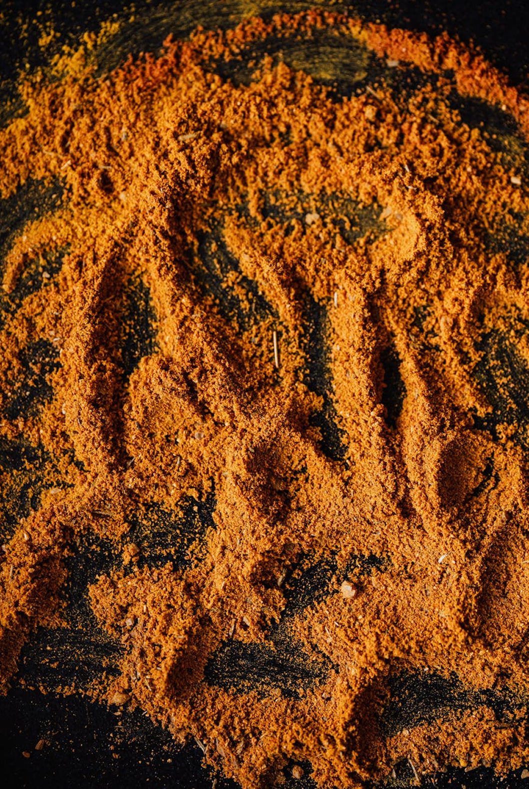 A close-up of a fine orange-brown powder, likely a spice blend or seasoning, spread across a dark textured surface.
